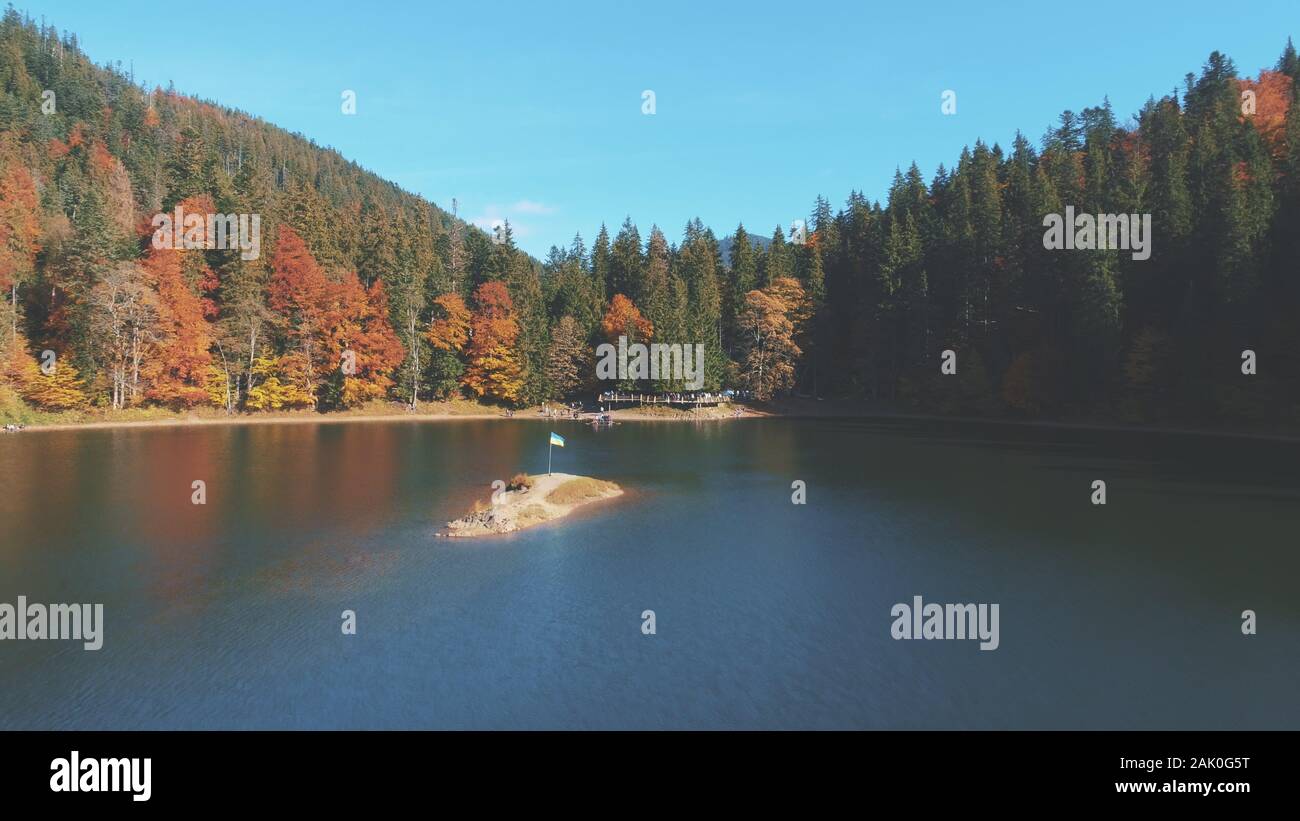 Ukrainische Flagge auf felsigen Insel in der Mitte des blauen ruhigen See von grünen und braunen gemischten Bäumen umgeben oberen Blick. Karpaten Berge, Ukraine Schönheit Natur. Reisen, Sommerferien. Stockfoto