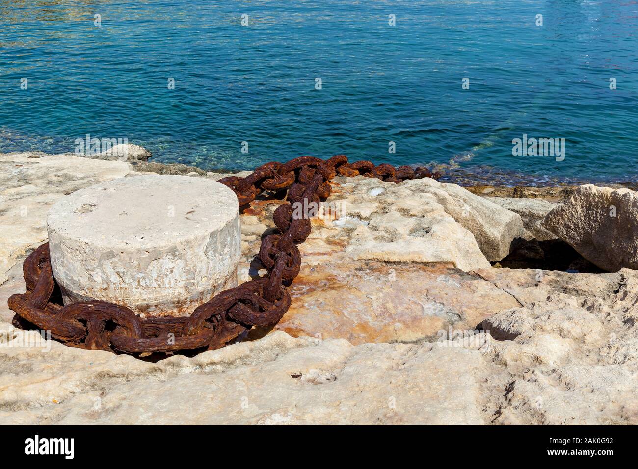 Nahaufnahme der Stein Poller mit einem alten rostigen Kette auf dem blauen Wasser Hintergrund. Stockfoto