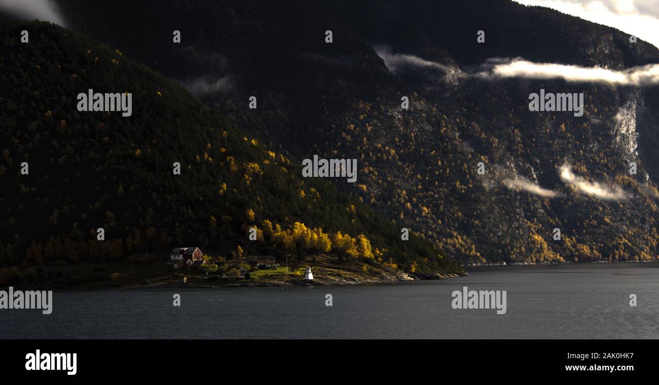 Bauernhof und Leuchtturm am Ufer des Herbst Fjord mit niedrigen Wolken Stockfoto