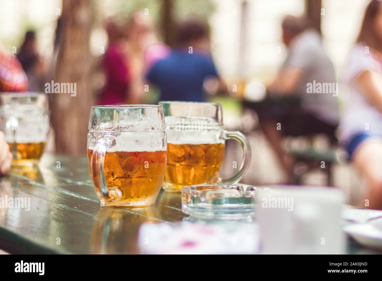 Gläser Bier im Gartenrestaurant, im Hintergrund sitzende Leute Stockfoto