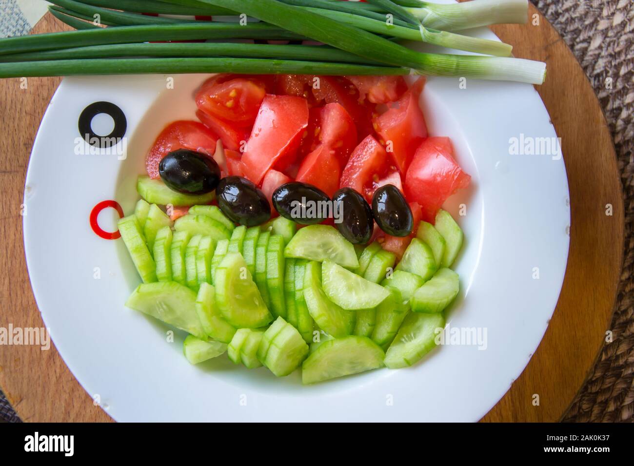 Salat mit frischem Gemüse, Gurken, Tomaten und schwarzen Oliven in einer Platte zum Würzen bereit, Zutaten für eine gesunde Ernährung Stockfoto