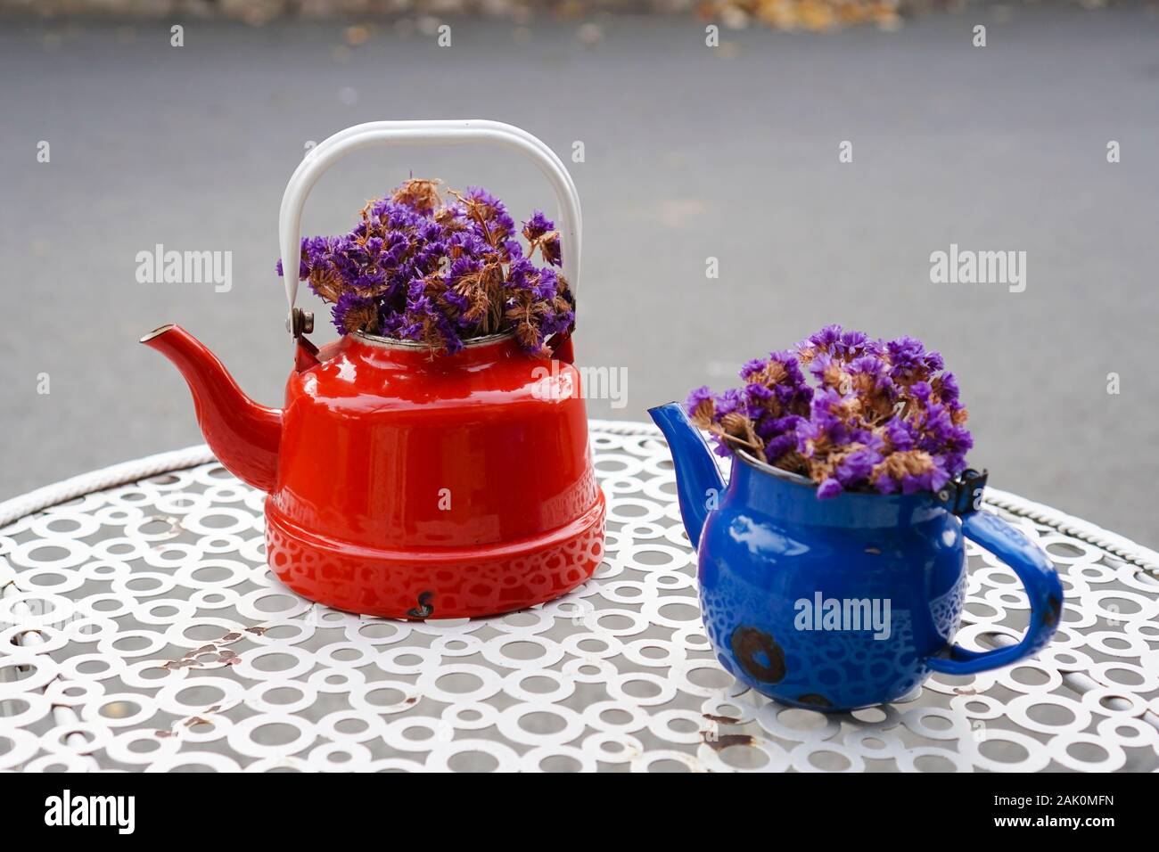 Vintage Teekannen sind auf einem Metall Gartentisch, mit violetten trockene Blumen innen als dekorative Objekte. Stockfoto