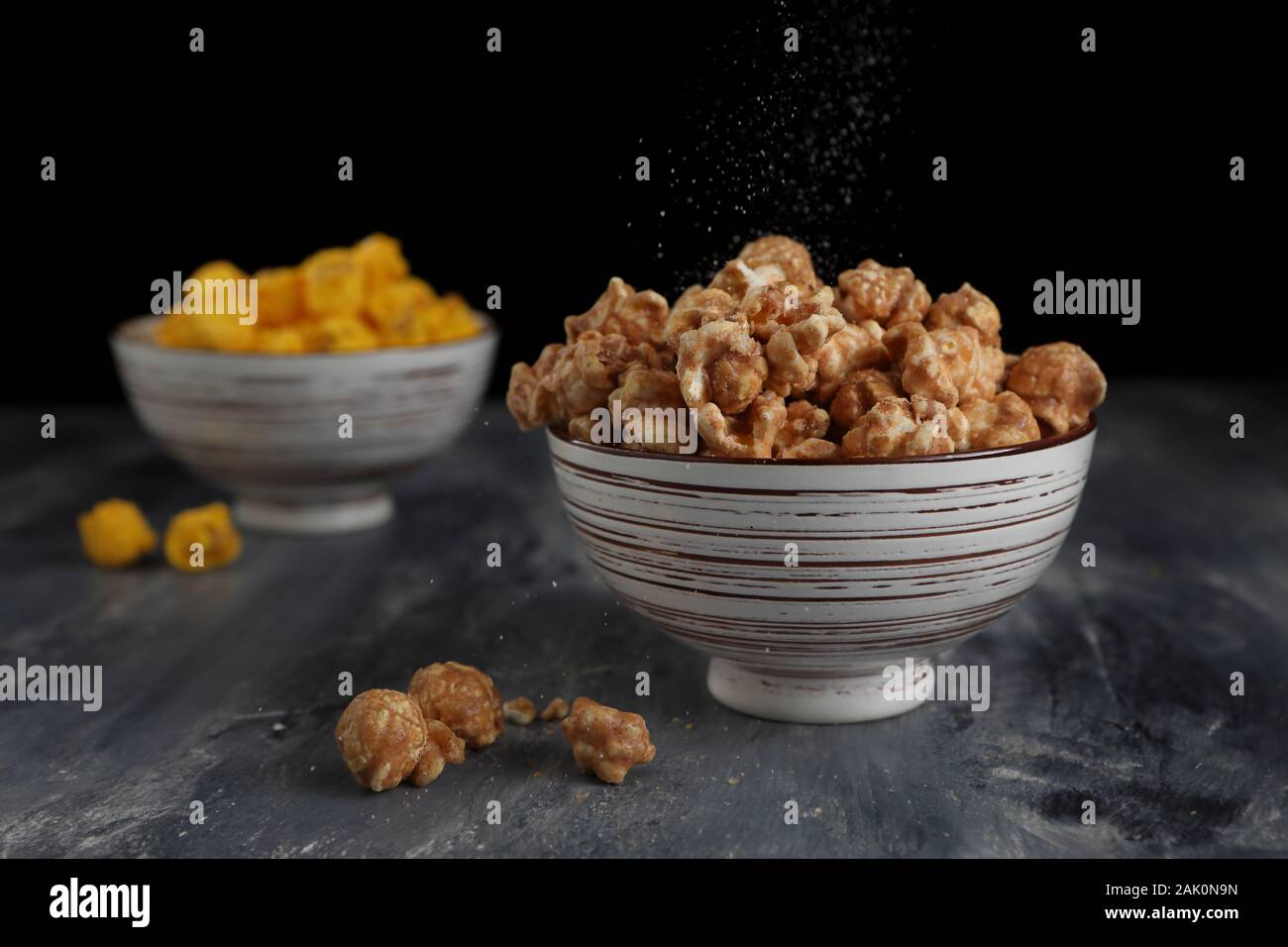 Eine Nahaufnahme von Salz streuen über Karamell Popcorn in eine Schüssel im Studio aufgenommen. Stockfoto