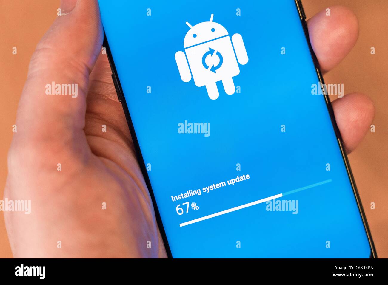 Eine Hand eines Mannes, die ein Smartphone hält, das ein Android-System-Update installiert und den Google Android-Maskottchen-Roboter - Bugdroid - zeigt Stockfoto