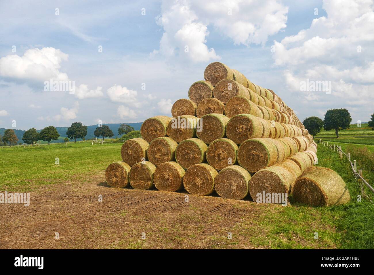 Stapel von Strohballen - runde Strohballen in einer Pyramide gestapelt, auf einem Feld, Allee und blauer Himmel mit weißen Wolken im Hintergrund Stockfoto
