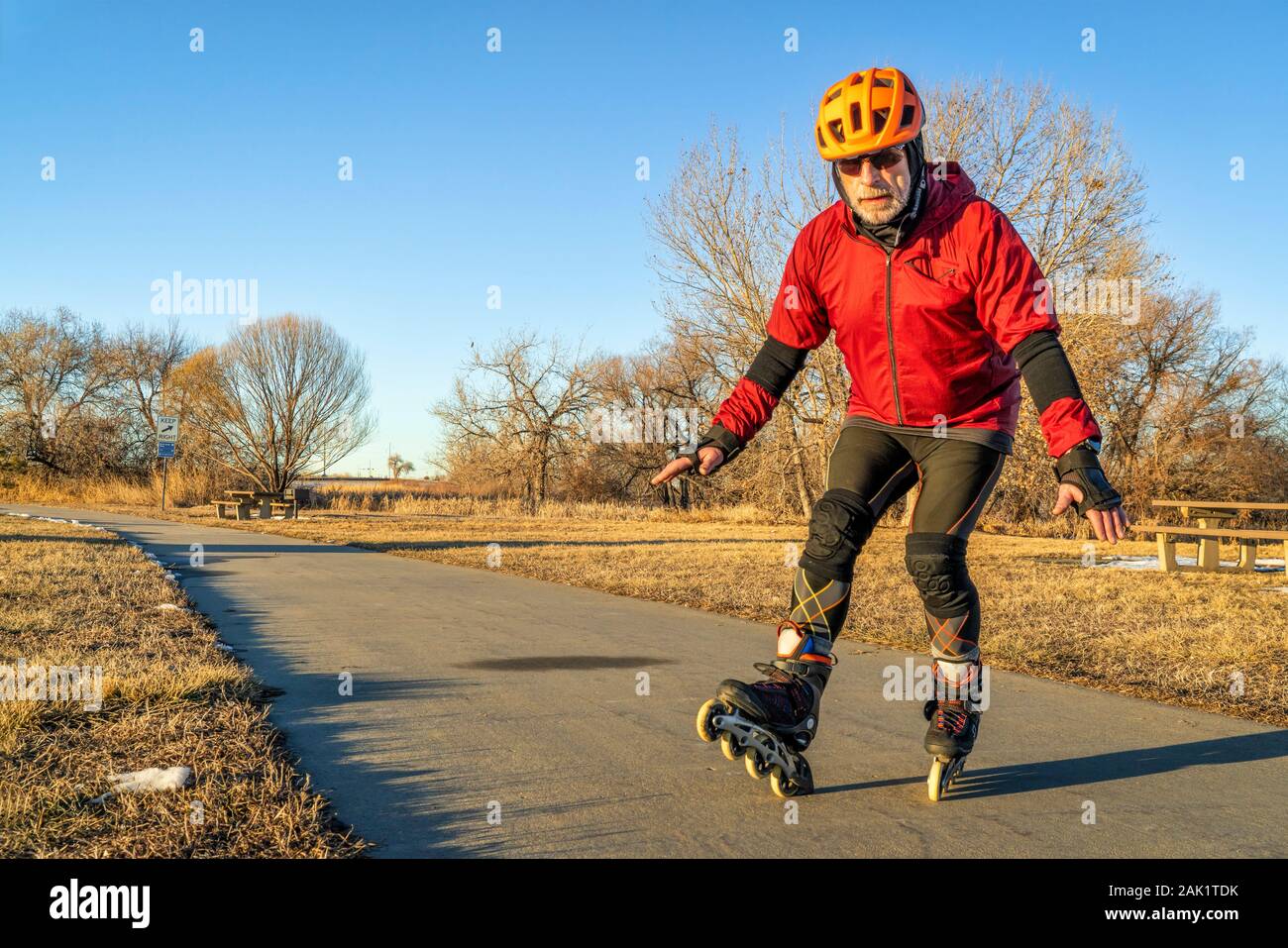 Senior athletischen Mann in Helm und Schutzkleidung wird Inline Skating auf einem asphaltierten Radweg - Boyd Lake Trail im Norden von Colorado im Winter Landschaft Stockfoto