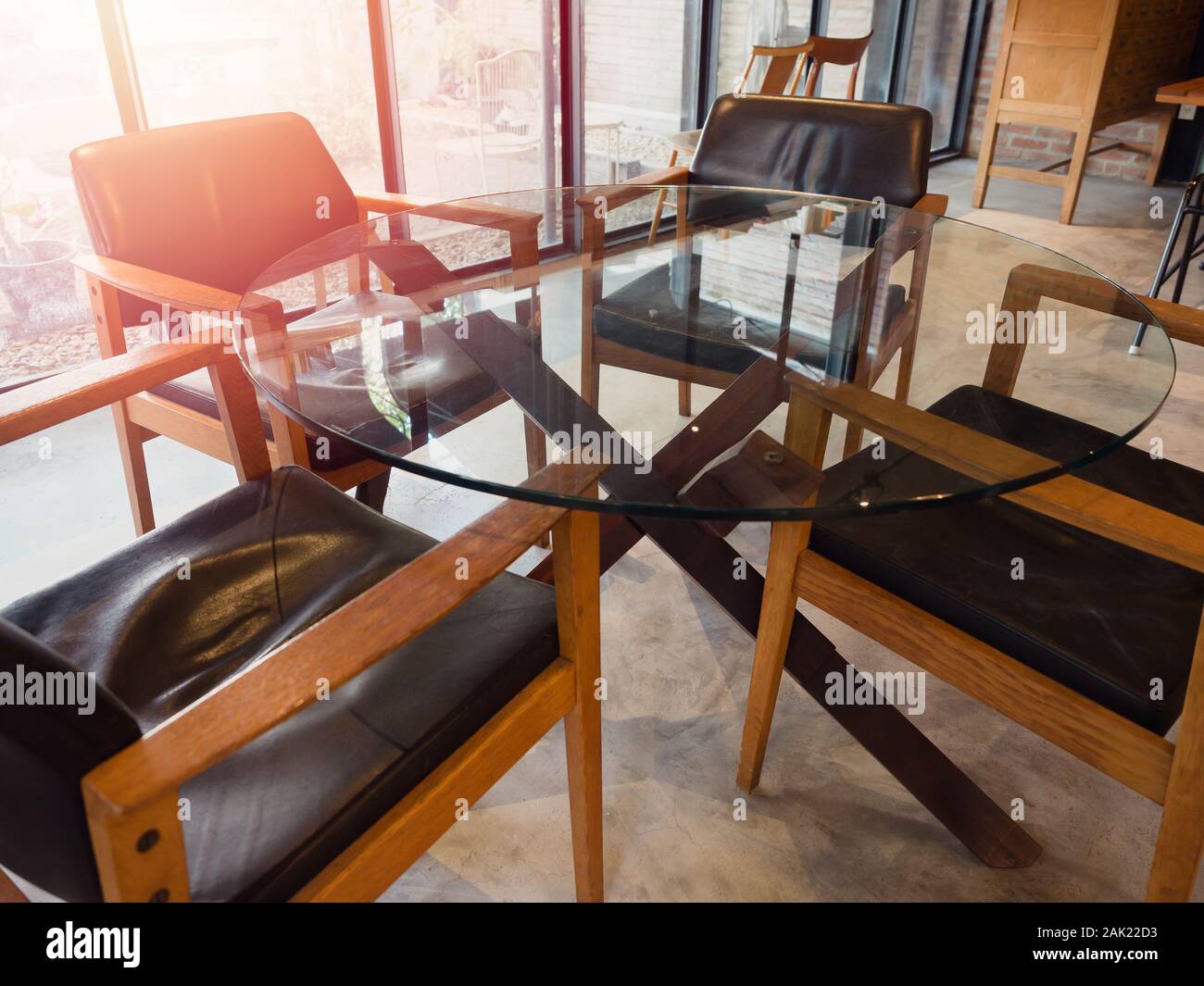 Moderne runder Glastisch mit 4 Stühlen aus Holz im Wohnzimmer loft Stil in der Nähe von Fensterglas mit Sonnenlicht von außen. Stockfoto