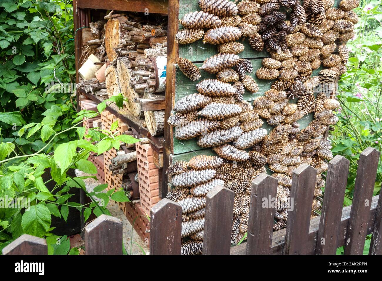 Großes Insektenhotel in einem bewachsenen Garten Holzhaufen Insekten, Zufluchtsort für Nützlinge, Ein Unterschlupf aus verschiedenen Materialien, Kegel, Stiele ... Stockfoto