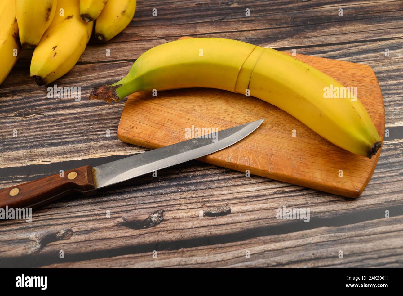 Eine reife, gelbe Banane schneiden sie in mehreren Teilen auf einem  Holzbrett und ein Messer auf einem Holz- Hintergrund. Nahaufnahme  Stockfotografie - Alamy