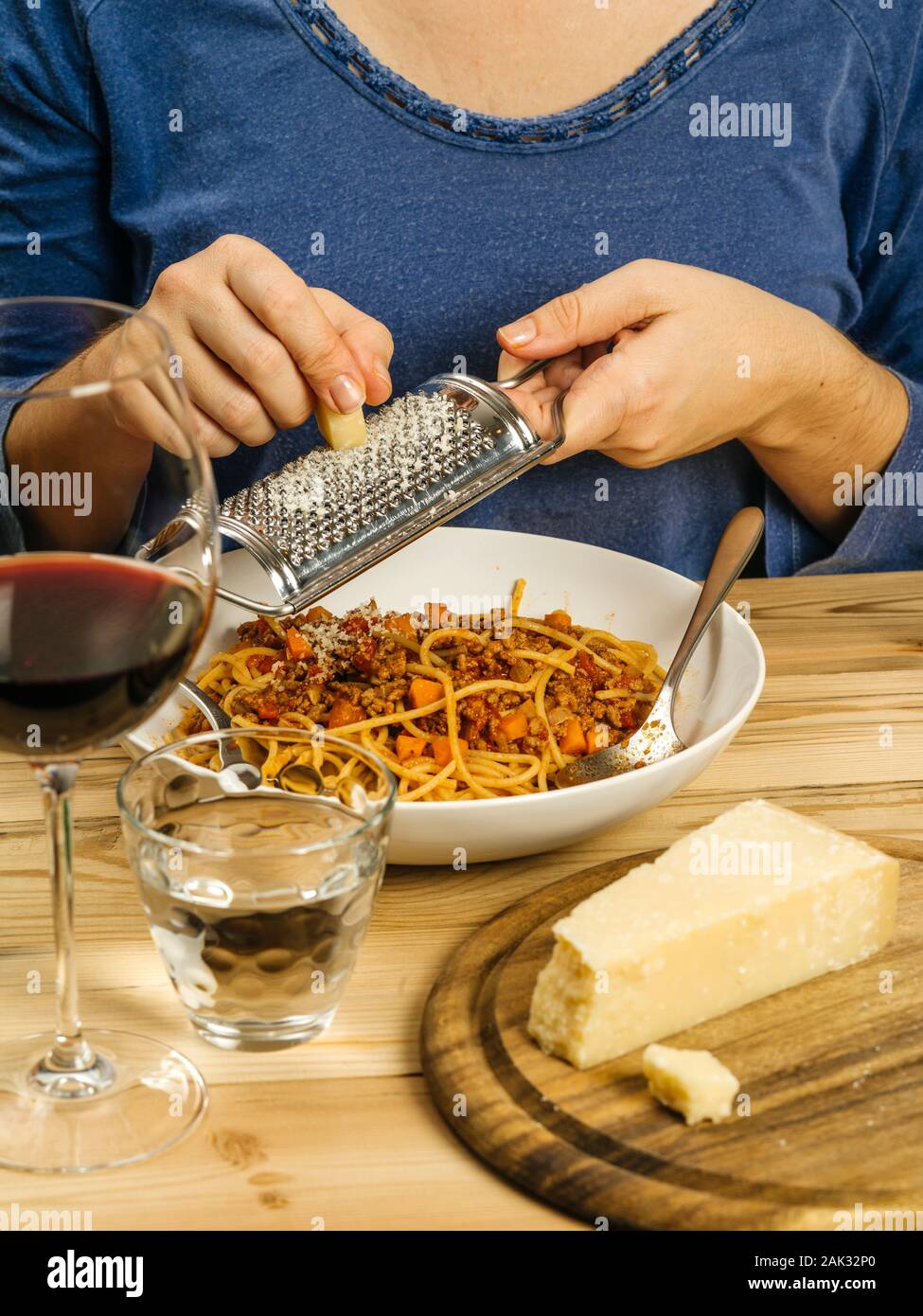 Foto einer Frau Gitter Parmesan über einer Schüssel der traditionellen Spaghetti Bolognese mit einem Glas Rotwein. Stockfoto