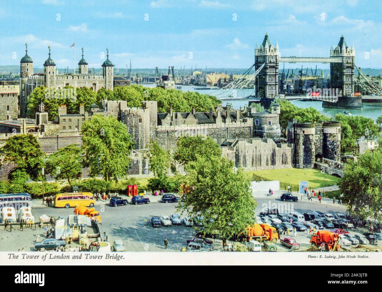 Eine historische Postkarte aus den 1950er und 60er Jahren des London Tower, der London Bridge und der Themse mit einem Parkplatz voller Autos und Touristenbusse im Vordergrund Stockfoto