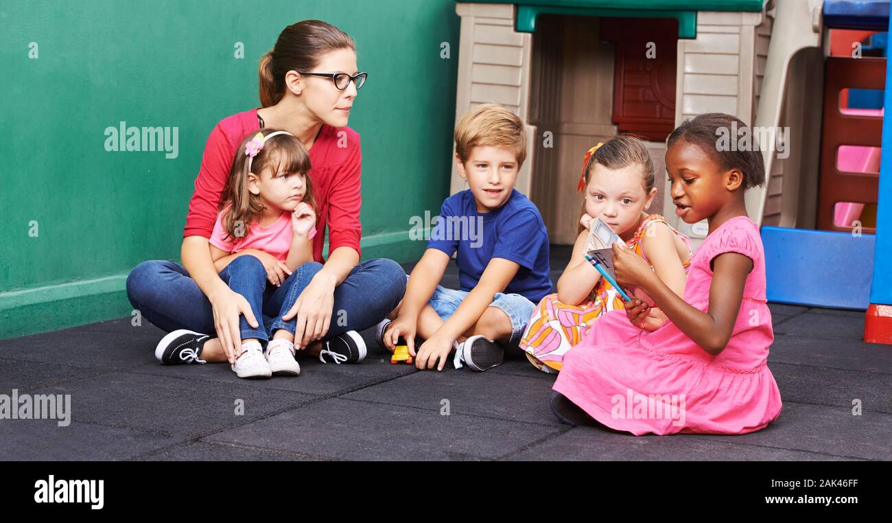 Kinder im Kindergarten Blick auf ein Bilderbuch mit der Erzieher Stockfoto