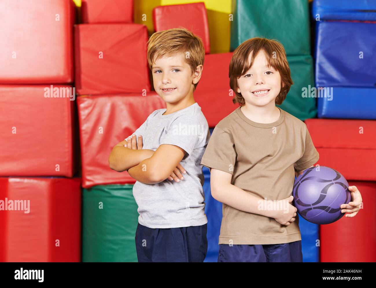 Zwei lächelnde Kinder stehen mit einer Kugel in der Turnhalle einer Grundschule Stockfoto