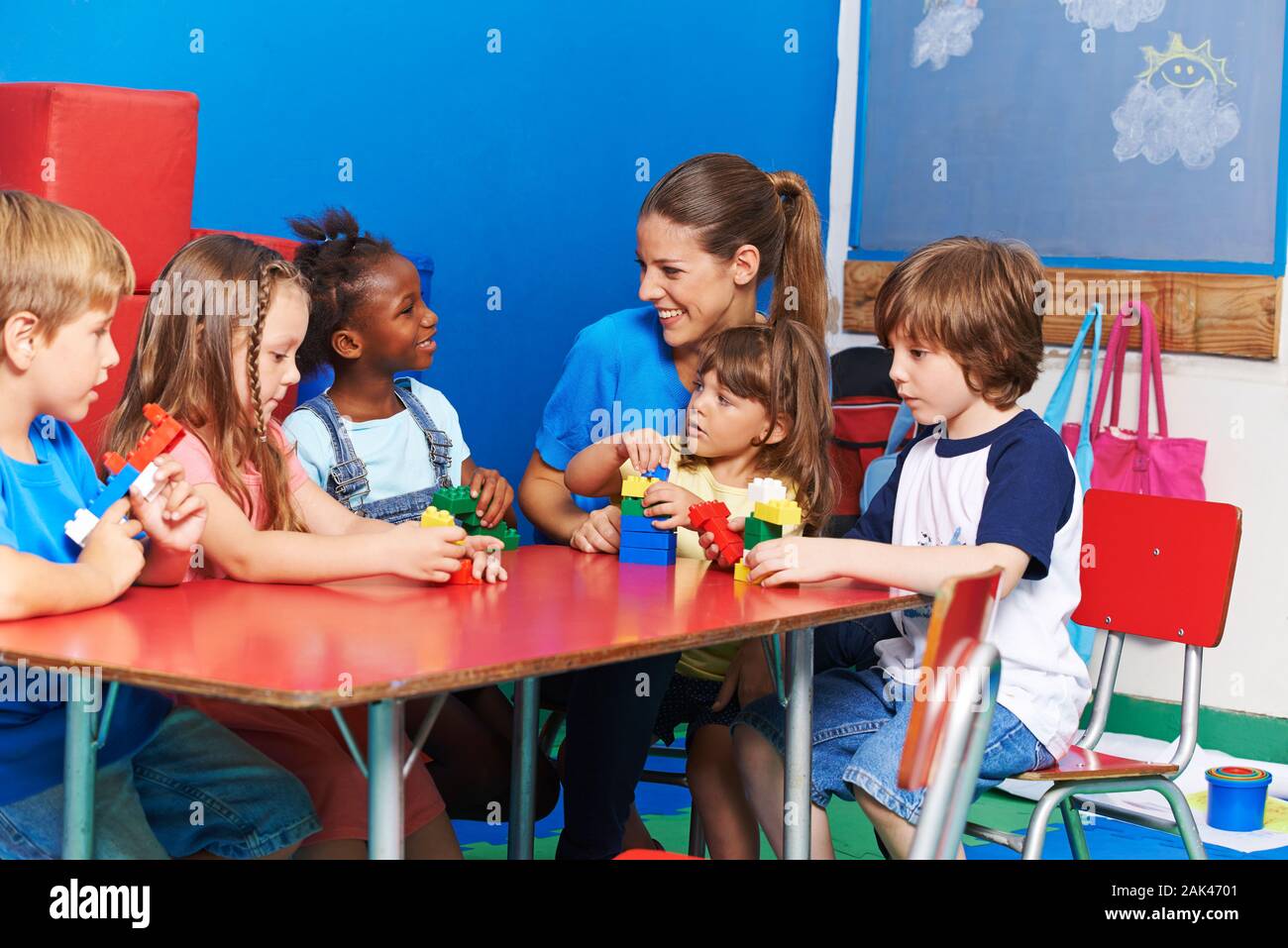 Kinder sitzen an einem Tisch mit Bausteine mit einem Lachen Erzieherin im Kindergarten Stockfoto