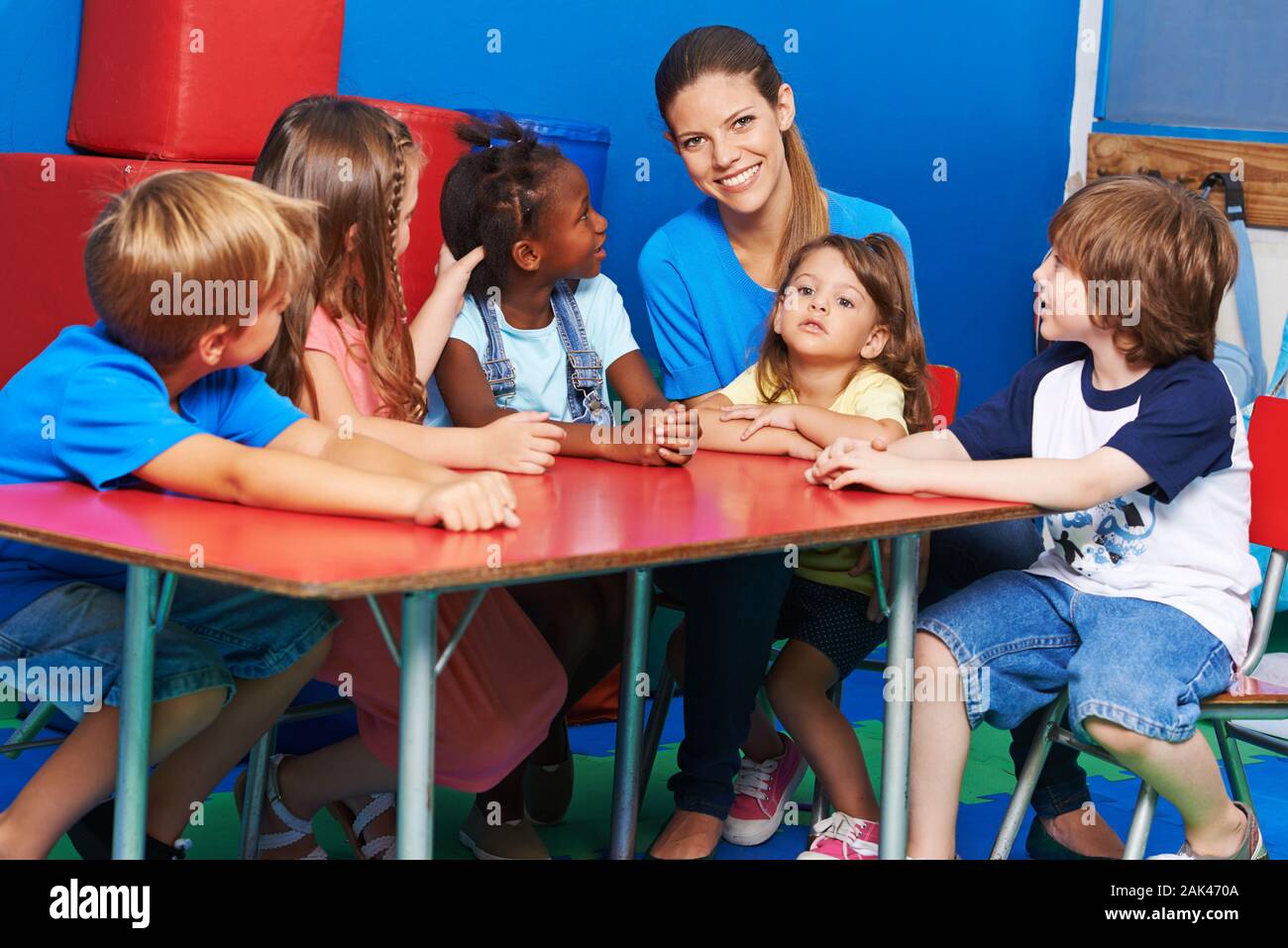 Happy Gruppe von Kindern sitzt mit einem lächelnden Erzieherin im Kindergarten am Tisch Stockfoto