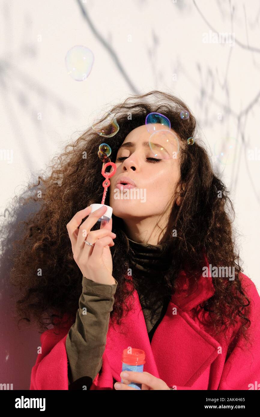 Junge Frau mit lockigem Haar im schicken Kleid bläst Seifenblasen Stockfoto