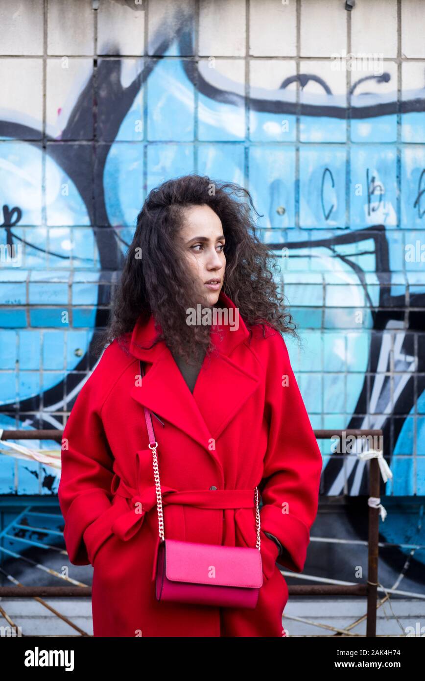 Junge Frau mit lockigem Haar im schicken Kleid Außenaufnahme gegen Graffiti, Wand Stockfoto