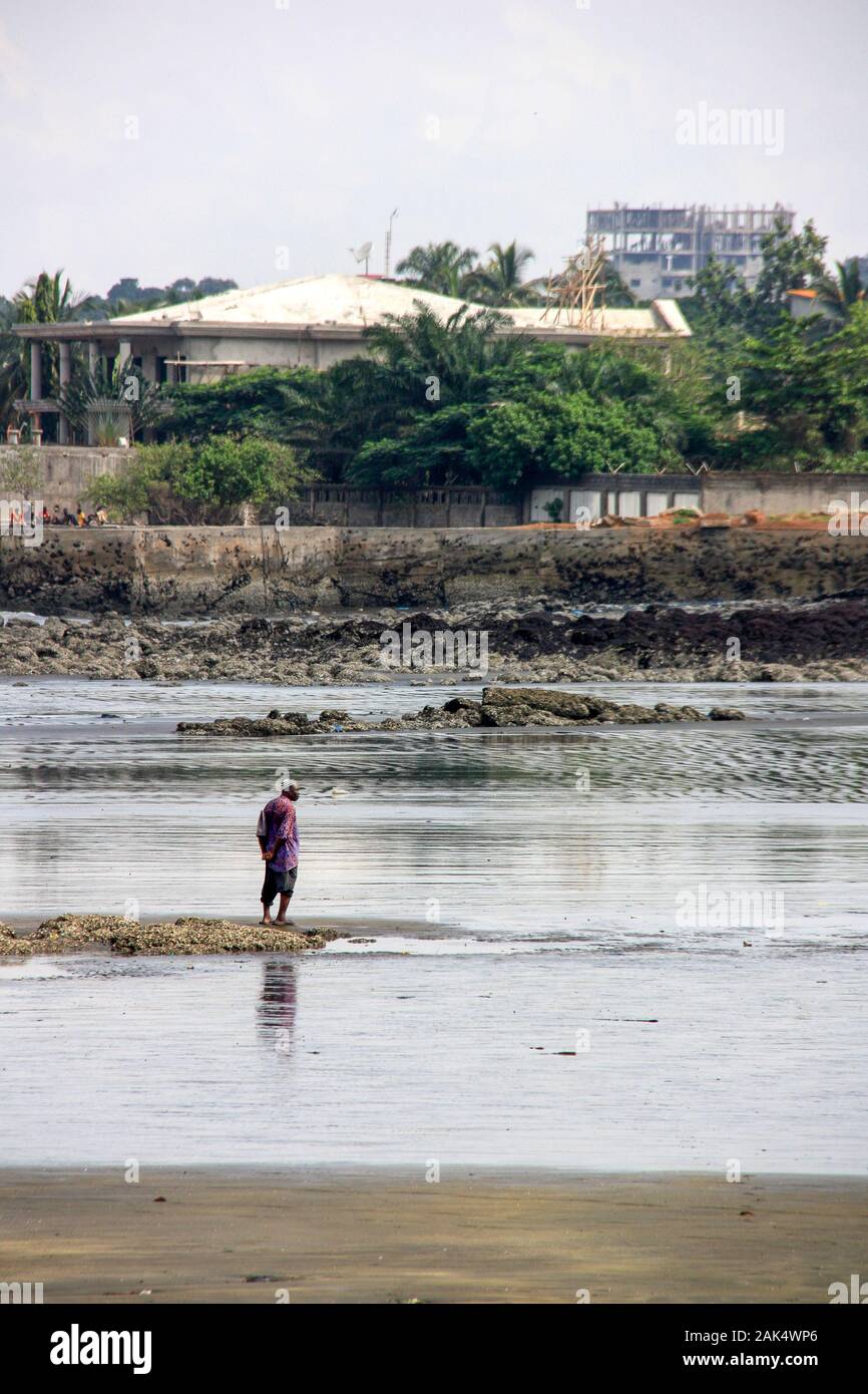 Ein alter Mann, der am Strand steht und die Szene am Strand in Conakry, Guinea, Westafrika beobachtet Stockfoto