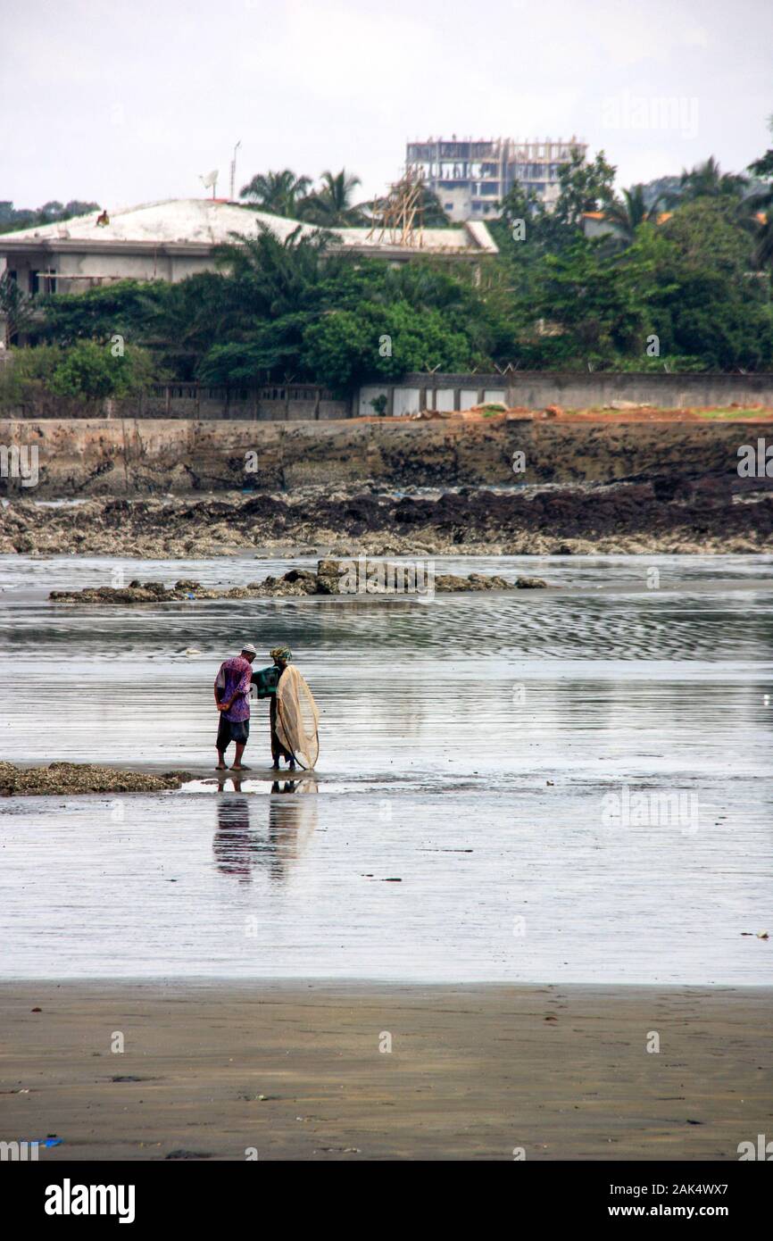 Fischerin aus der Region, die mit dem Fang des Tages vom Fischfang zurückkehrt und es einem älteren Mann am Strand in Conakry, Guinea, zeigt Stockfoto
