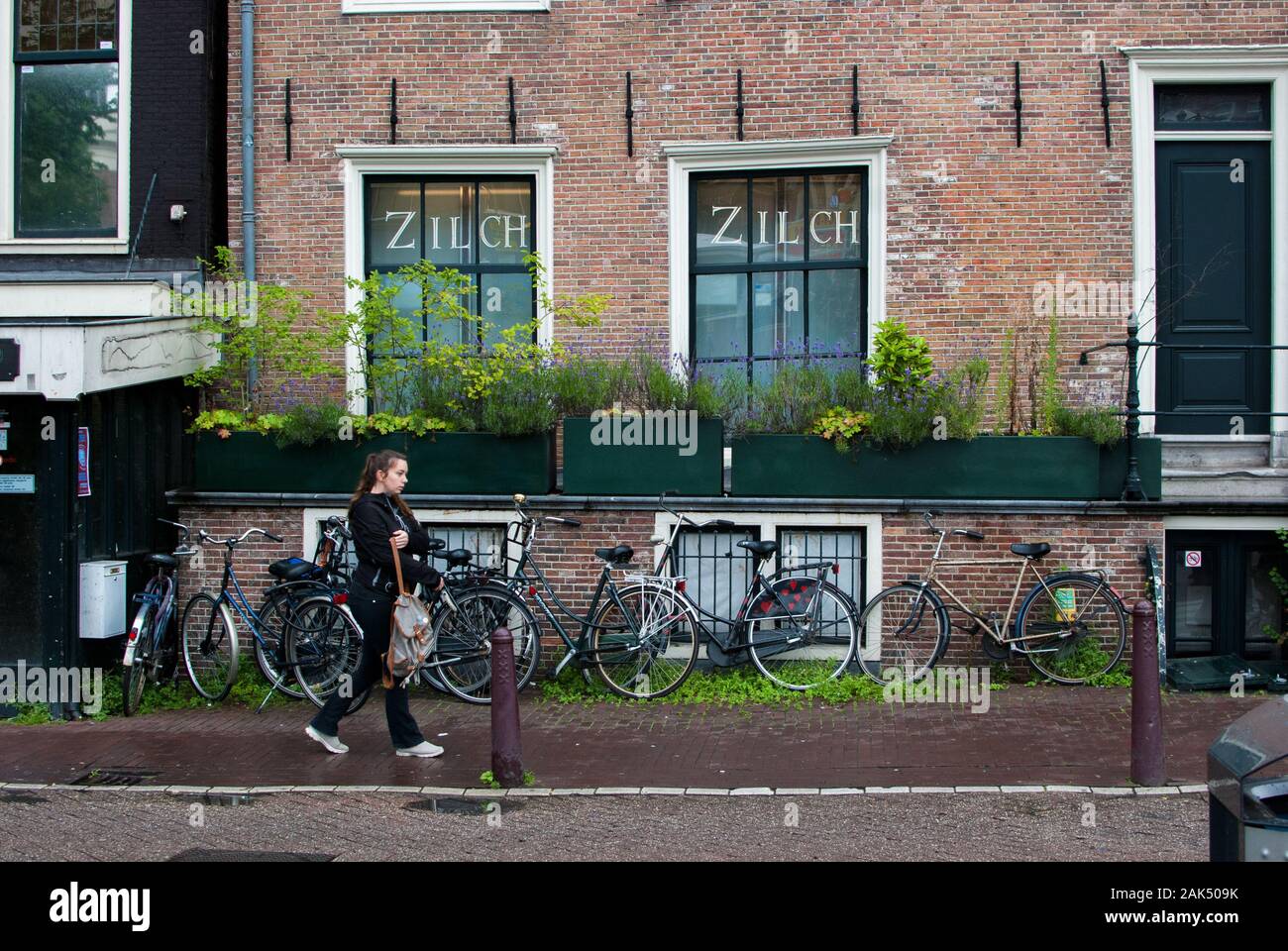 Frau zu Fuß auf dem Gehweg in Schwarz mit vielen Fahrrädern auf dem Hintergrund geparkten gekleidet Stockfoto
