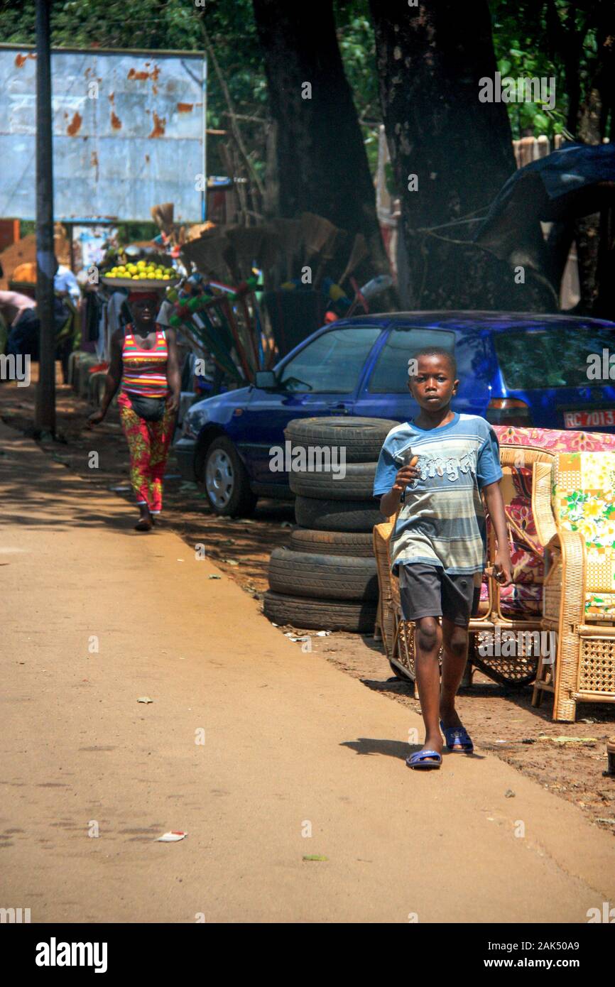 Afrikanischer Junge, der auf der Seite einer Feldstraße in Conakry, Guinea, Westafrika, spaziert Stockfoto