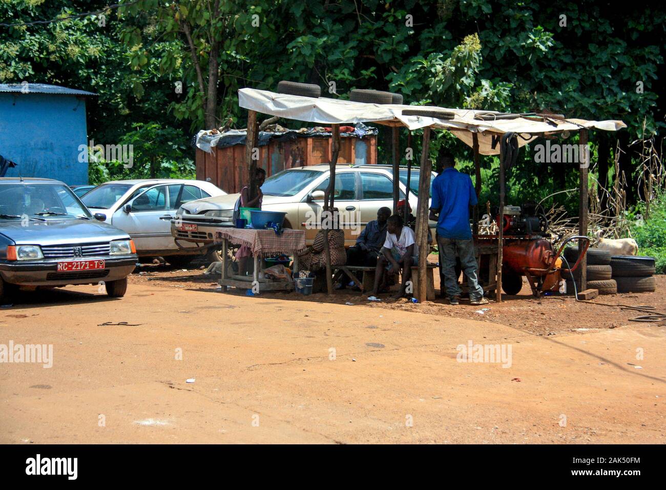Menschen, die im Schatten einer sehr einfachen Garage in Conakry, Guinea, Westafrika sitzen Stockfoto