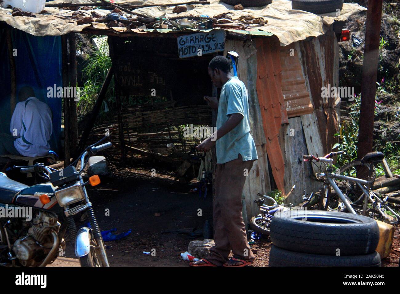Afrikanischer Mann, der in einer Wellblechscheune in Conakry eine sehr einfache Motorradwerkstatt betritt, Stockfoto