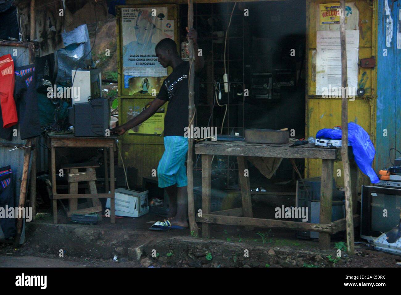 Blick auf einen Mann vor einem kleinen und sehr einfachen Elektronikladen in Conakry, Guinea, Westafrika, mit dem Kunden erwartet werden Stockfoto
