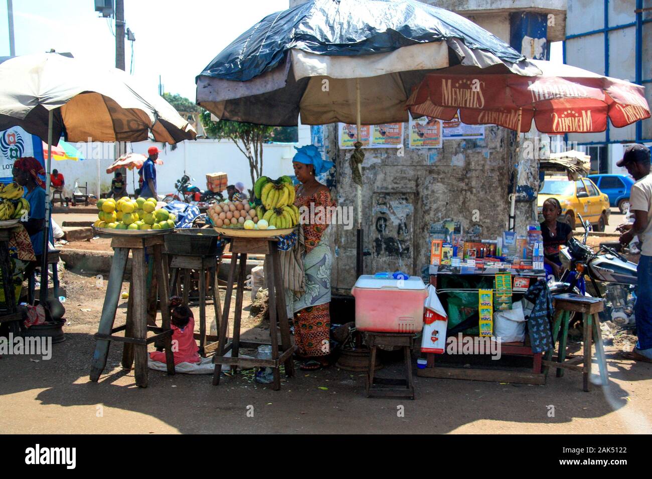 Blick auf eine lokale Frau, die Obst, Gemüse, Eier und Süßigkeiten an einem einfachen Marktstand neben der Straße in Conakry, Guinea, verkauft Stockfoto