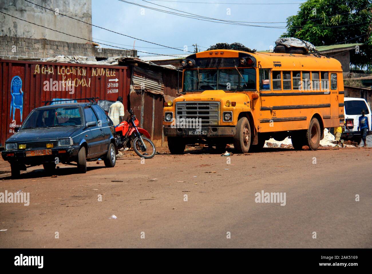 Außenansicht eines geklatschten orangefarbenen amerikanischen Schulbusses, der an der Schulter der Hauptstraße durch Conakry, Guinea, Westafrika geparkt ist Stockfoto