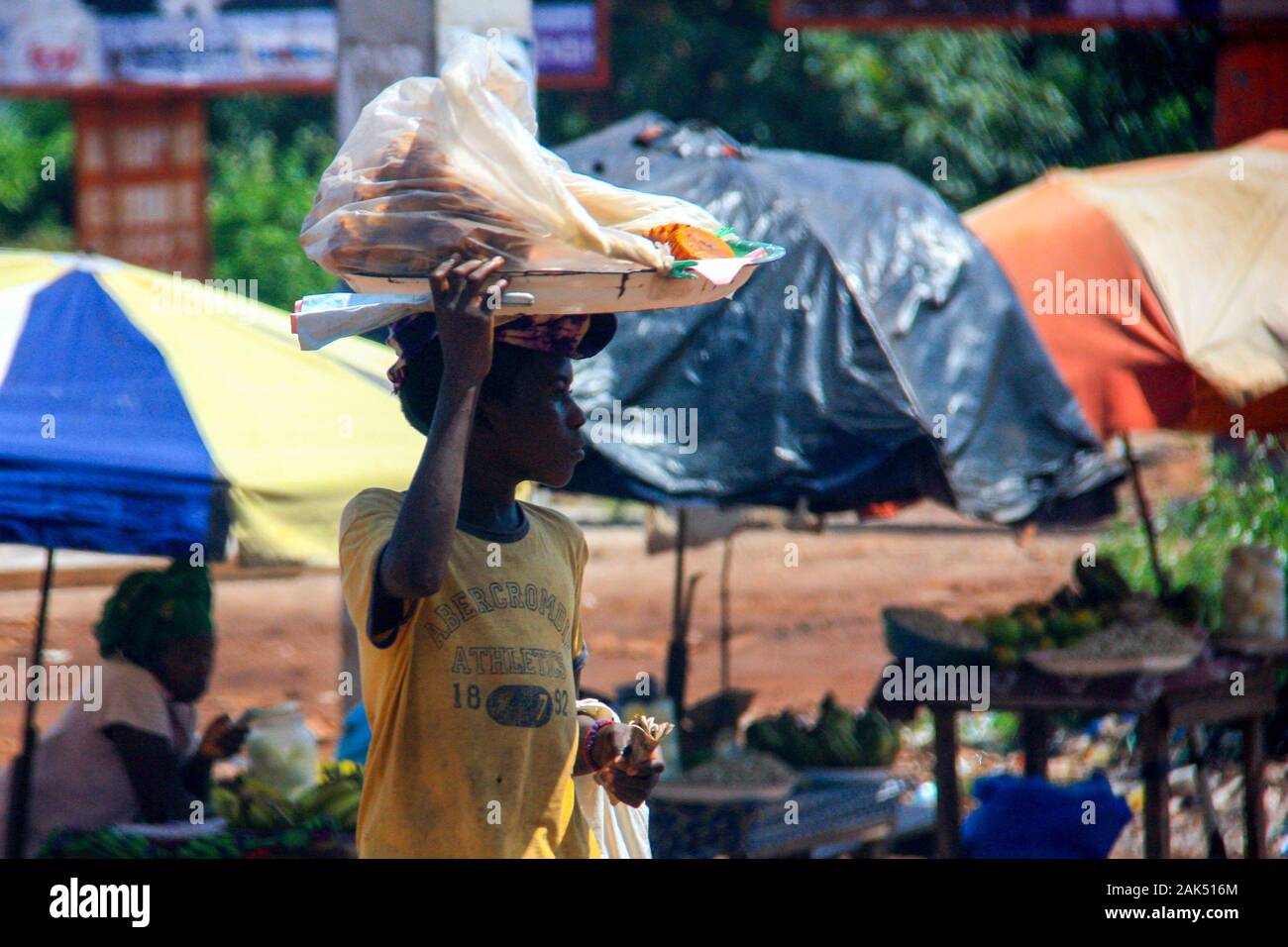 Die Afrikanerin balanciert ihre Waren auf dem Kopf und wartet darauf, dass Autos an der Seite der Straße anhalten - Conakry, Guinea Stockfoto