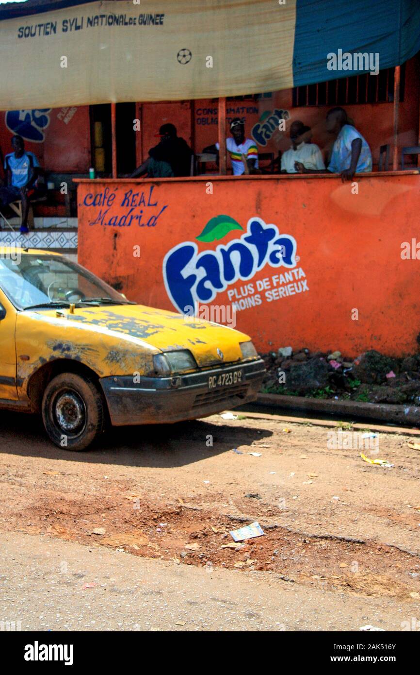 Blick auf ein altes gelbes Auto, das auf der Seite der Feldstraße vor dem Café Real Madrid in Conakry, Guinea, geparkt ist Stockfoto