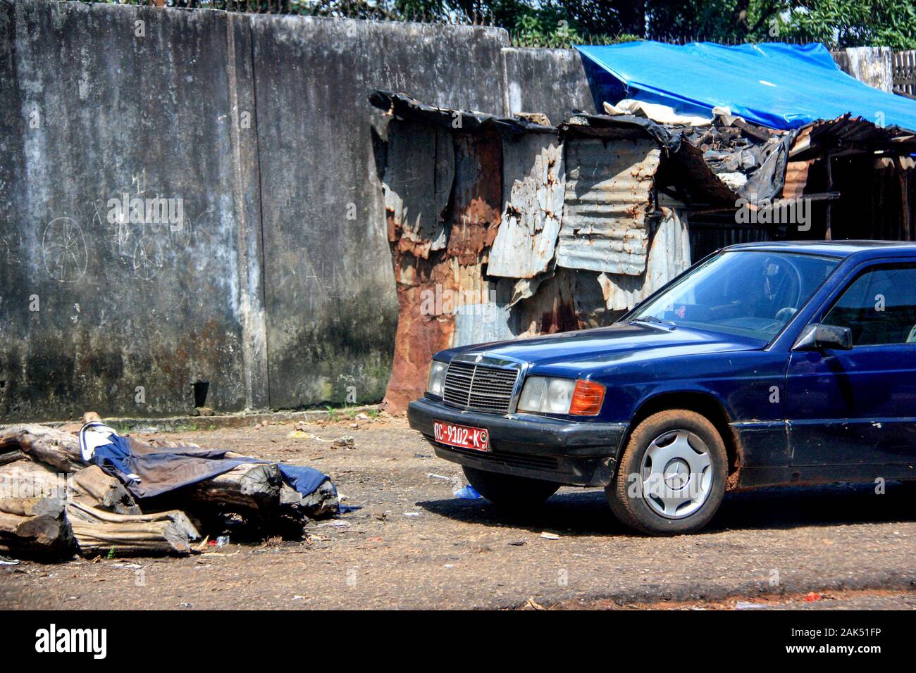 Außenansicht eines alten blauen Mercedes-Wagens, der vor Wellblechbarnen in Conakry, Guinea, Westafrika geparkt ist Stockfoto