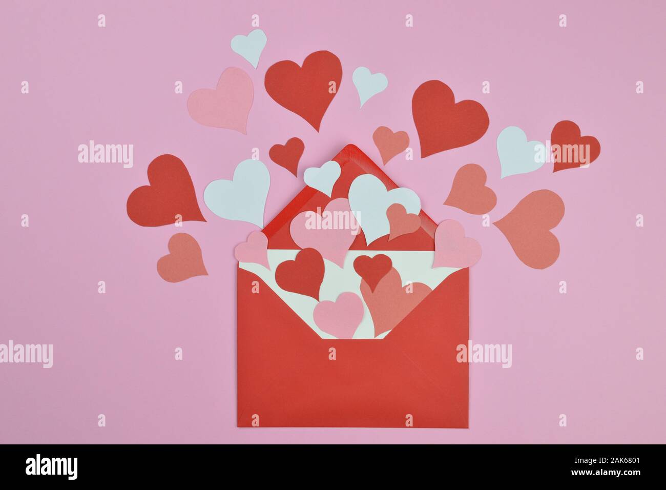 Weiße leere Schreiben in offenen roten Umschlag mit vielen verschiedenen rot, rosa und weißen Papier Herzen heraus kommenden verteilt auf rosa Hintergrund als Liebe schreiben Stockfoto