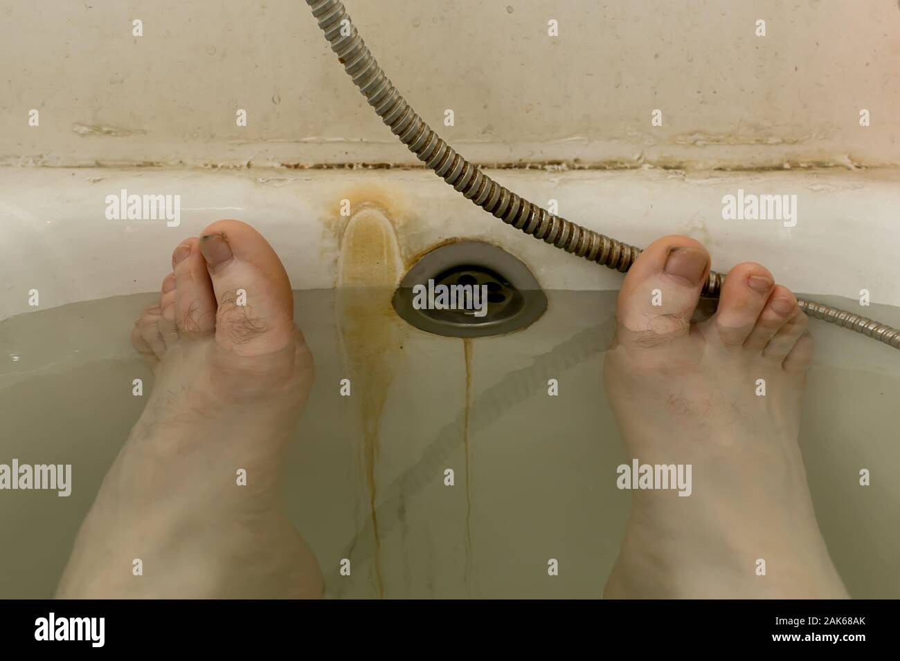 Menschliche Füße im Wasser im schmutzig rostigen Bad einer Gemeinschaftswohnung, unsanitäre Bedingungen, schlechte Lebensbedingungen Stockfoto