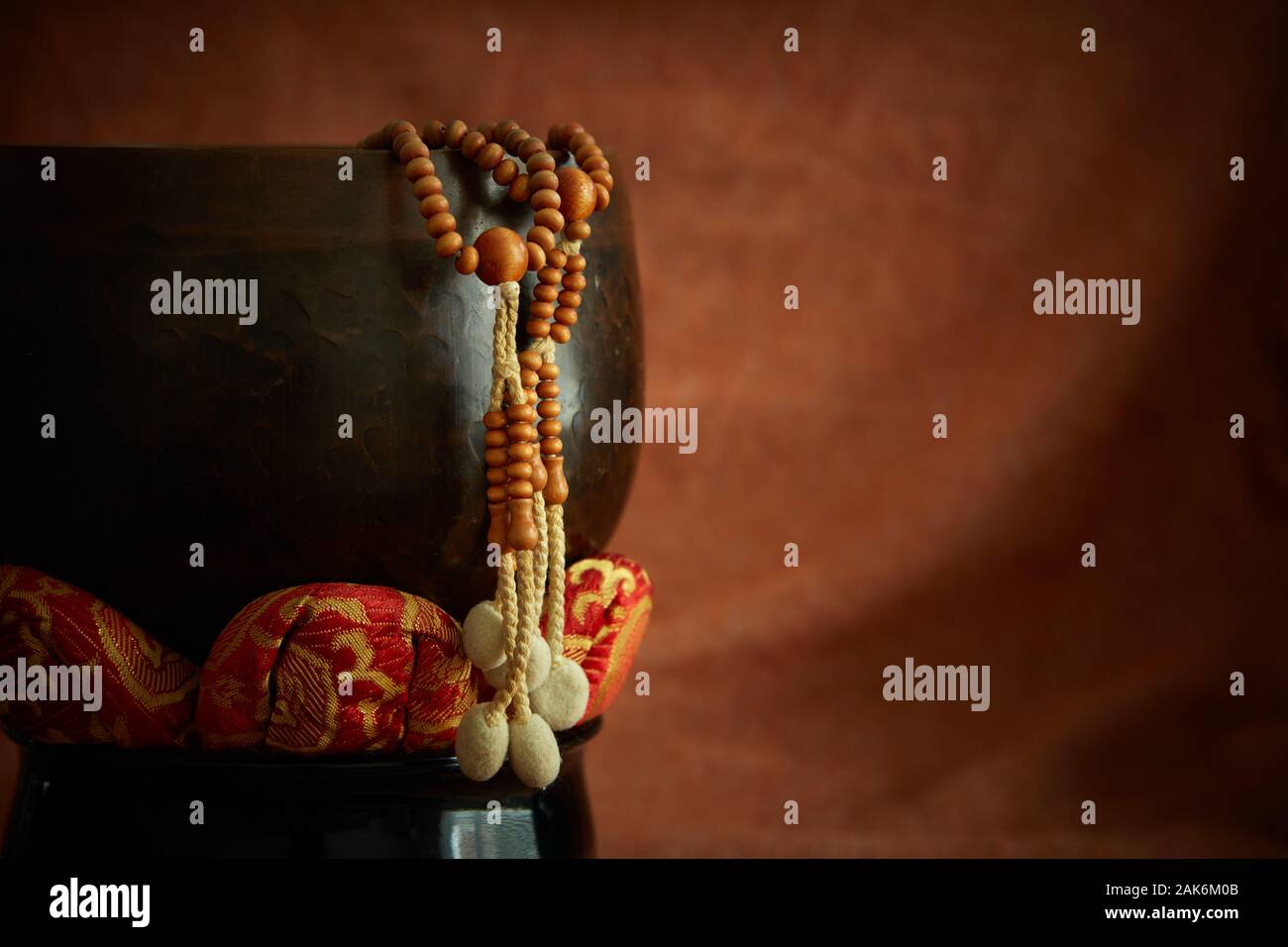 Buddhistische Juzu Gebetsperlen hängt über der Seite einer Glocke auf Lotus Kissen. Auf einem Tuch Hintergrund ähnlich wie die Farbe der gebrannte Sienna fotografiert. Stockfoto