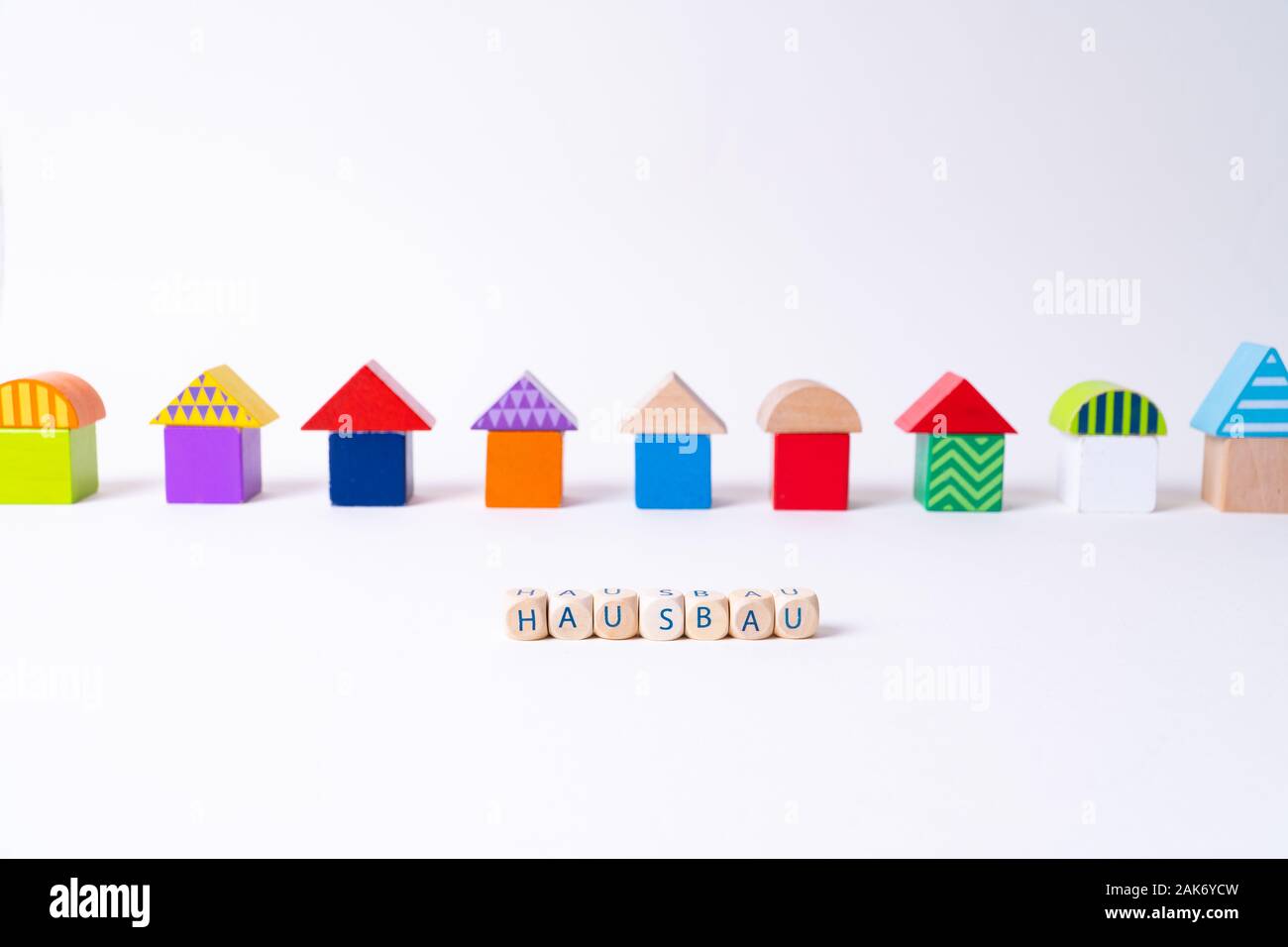 Würfel mit Buchstaben sagen 'Hausbau', das deutsche Wort für den Bau eines Hauses vor einer Reihe von Häusern gebaut von bunten Spielzeug Spielzeug Bausteine Stockfoto