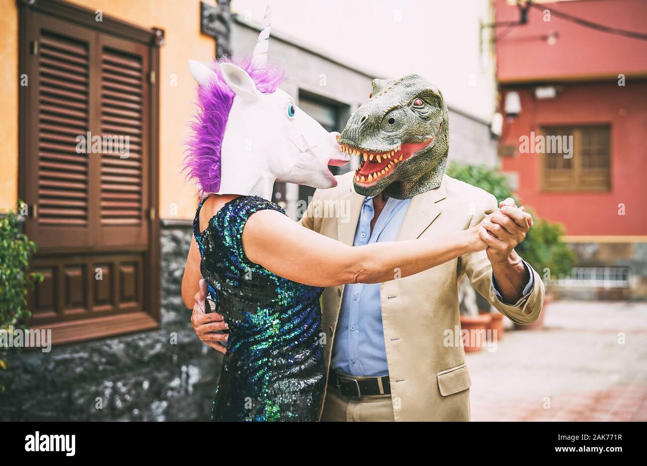 Verrücktes Paar tanzen und tragen Dinosaurier T-Rex und Einhorn Maske - Senior eleganten Menschen Spaß an Karneval Parade maskiert Stockfoto