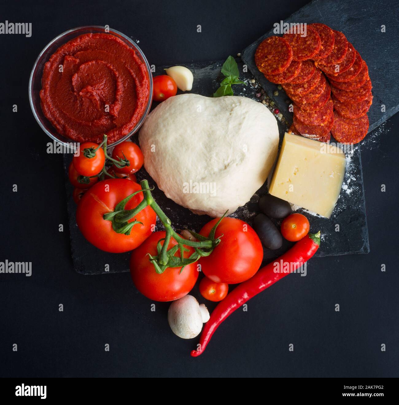 Rohen Teig für Pizza mit Zutaten und Gewürzen auf Schwarz tisch Hintergrund in Herzform liebe Essen der Valentinstag Konzept Stockfoto