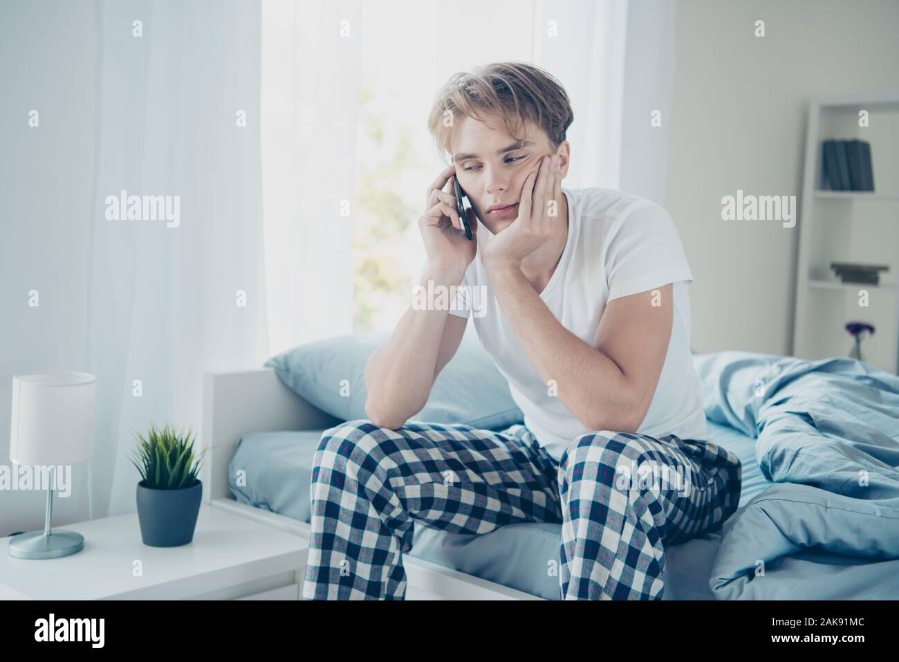 Portrait von müde, erschöpft, blonder Kerl sitzen auf dem Bett mit Handy seine Frau rufen nach harten Partei fühlen Kater Kopfschmerzen im Haus drinnen tragen Stockfoto