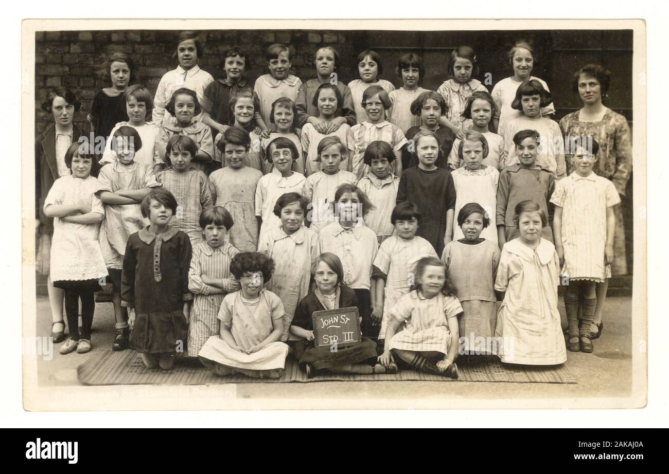 Anfang 1900 Schule Foto Postkarte von Kleinkind Mädchen und Lehrer an John Street Rat Schule, Salford, Lancashire, England, Großbritannien, circa 1920. Stockfoto