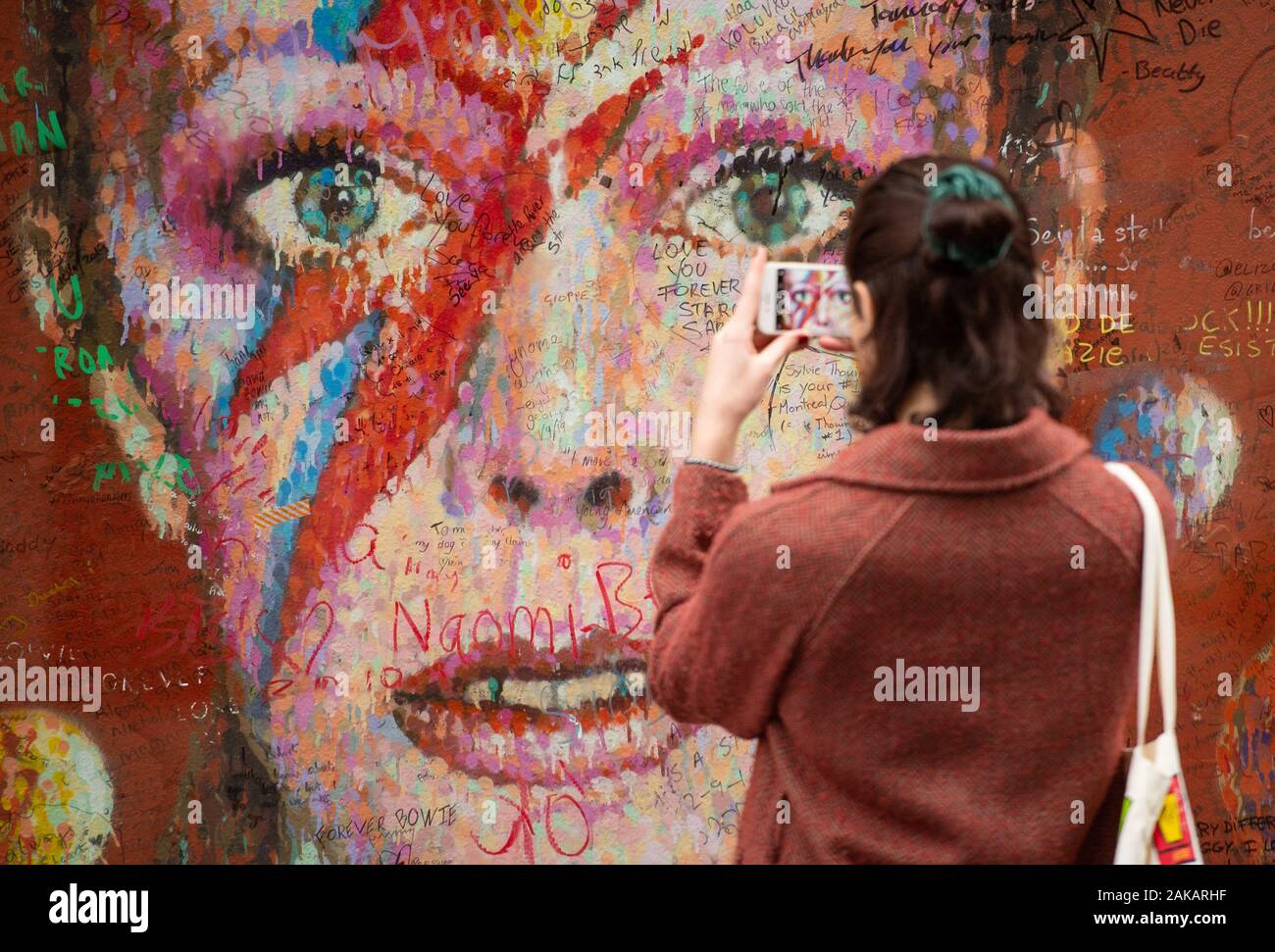 Eine Frau fotos Nachrichten auf dem David Bowie Wandbild in Brixton, London geschrieben, auf das, was der Sänger 73. Geburtstag gewesen wäre. Stockfoto