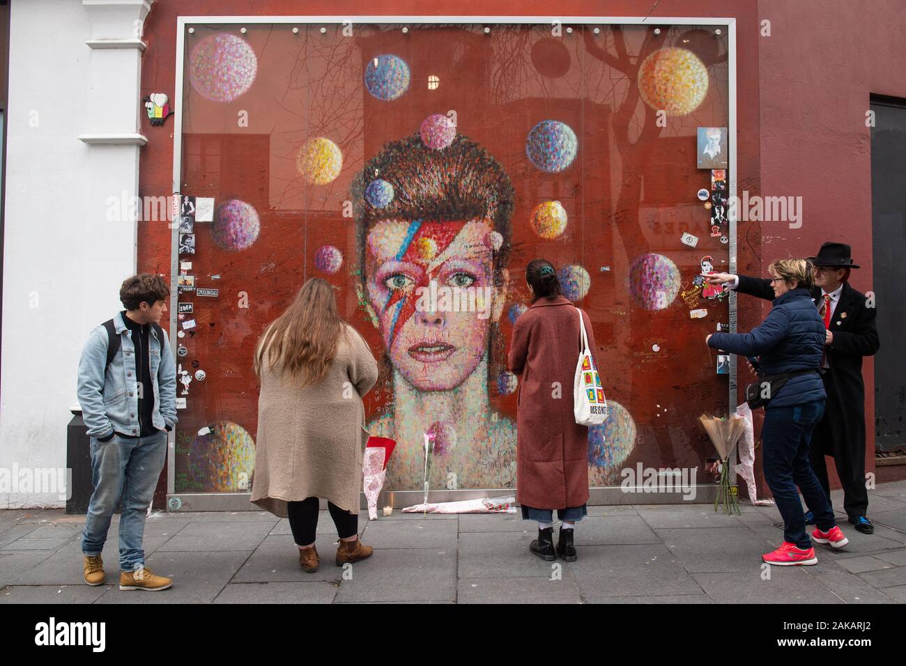 Die Menschen lesen die Nachrichten auf dem David Bowie Wandbild in Brixton, London geschrieben, auf das, was der Sänger 73. Geburtstag gewesen wäre. Stockfoto