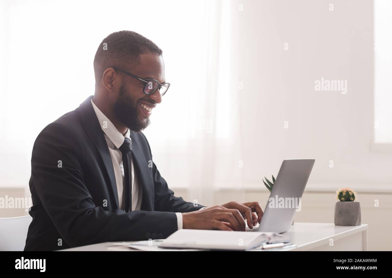 Afrikanische amerikanische Geschäftsmann arbeiten in modernen High-Tech-Büro, Schreibarbeiten auf Laptop, freier Speicherplatz, Seitenansicht Stockfoto