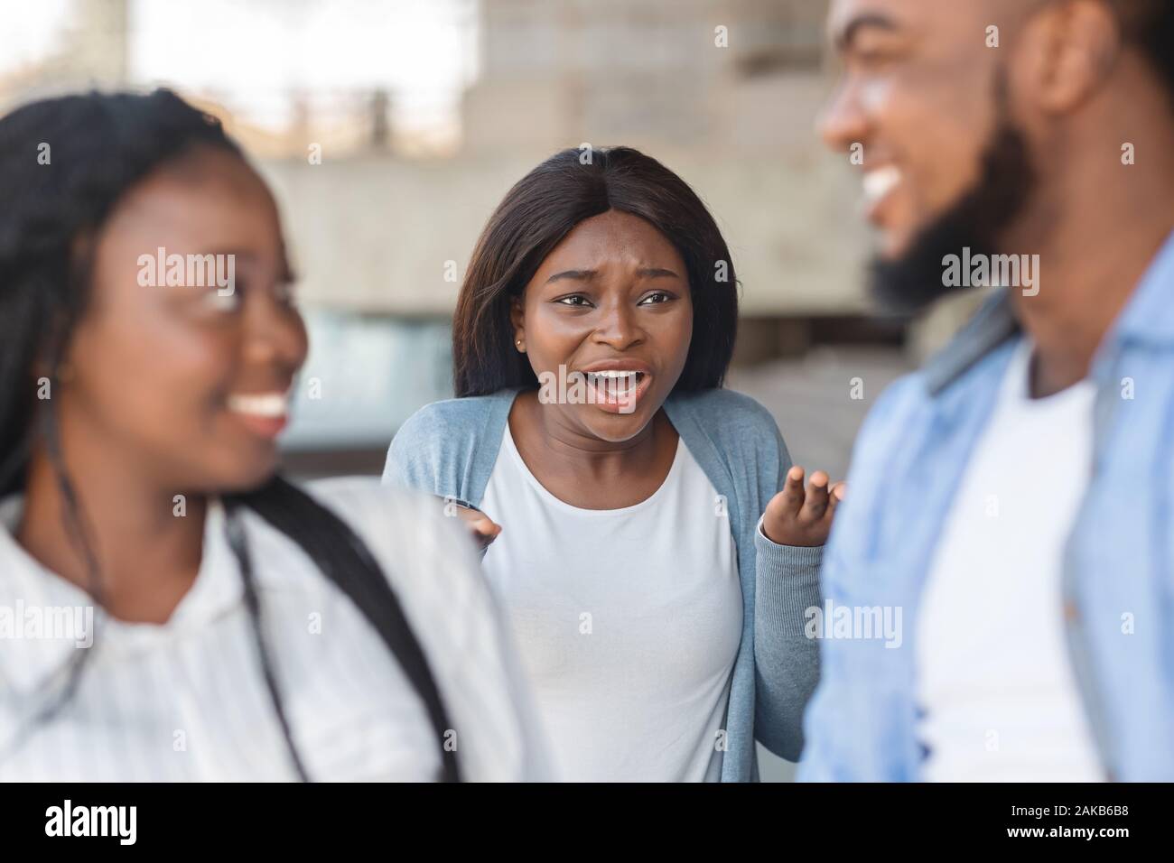 Eifersucht Konzept. Grumpy schwarze Mädchen wütend zu ihrem Freund, flirten mit einer anderen Frau, stehend mit wütenden Gesichtsausdruck auf Hintergrund Stockfoto