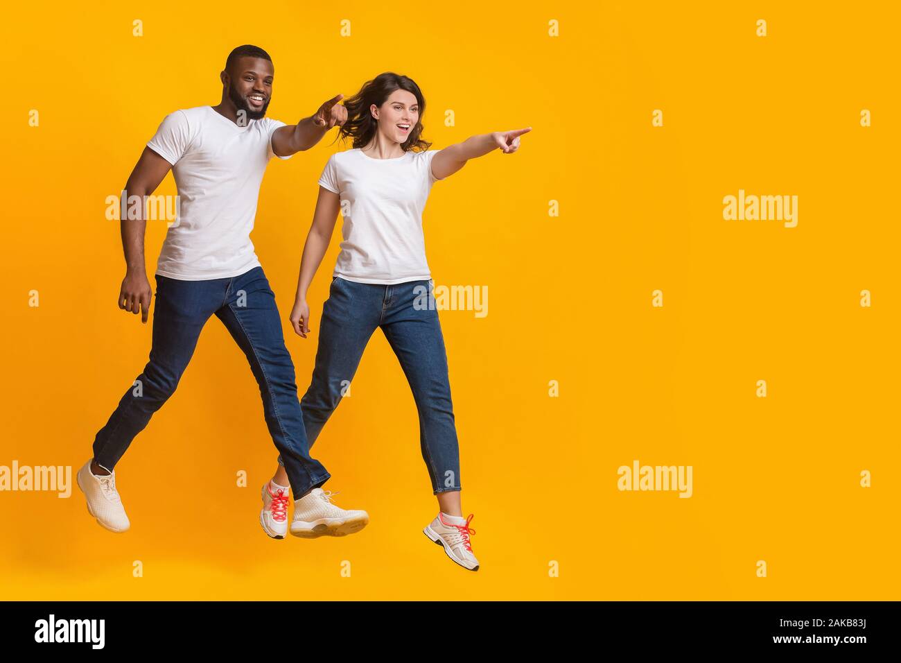 In die gleiche Richtung. Springen interracial Paare an der Kopie Raum über gelben Hintergrund zeigen, volle Länge geschossen Stockfoto