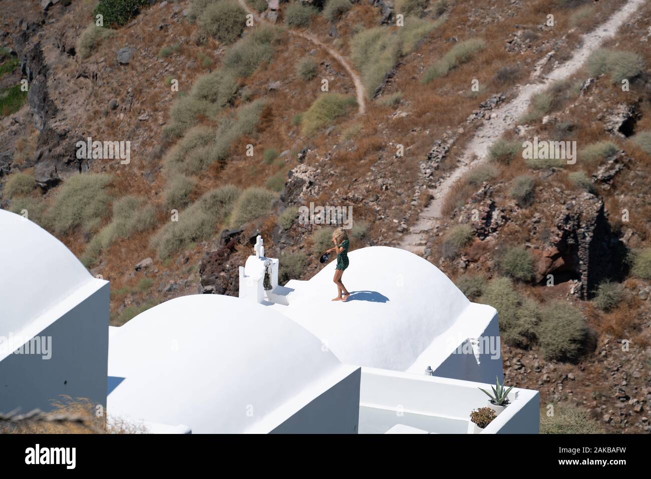 Santorini Griechenland - 10. August 2019; attraktive große Frau Schlachten der Wind auf geschwungene Dach der Weißen typisch griechische Insel Gebäude agai Stockfoto