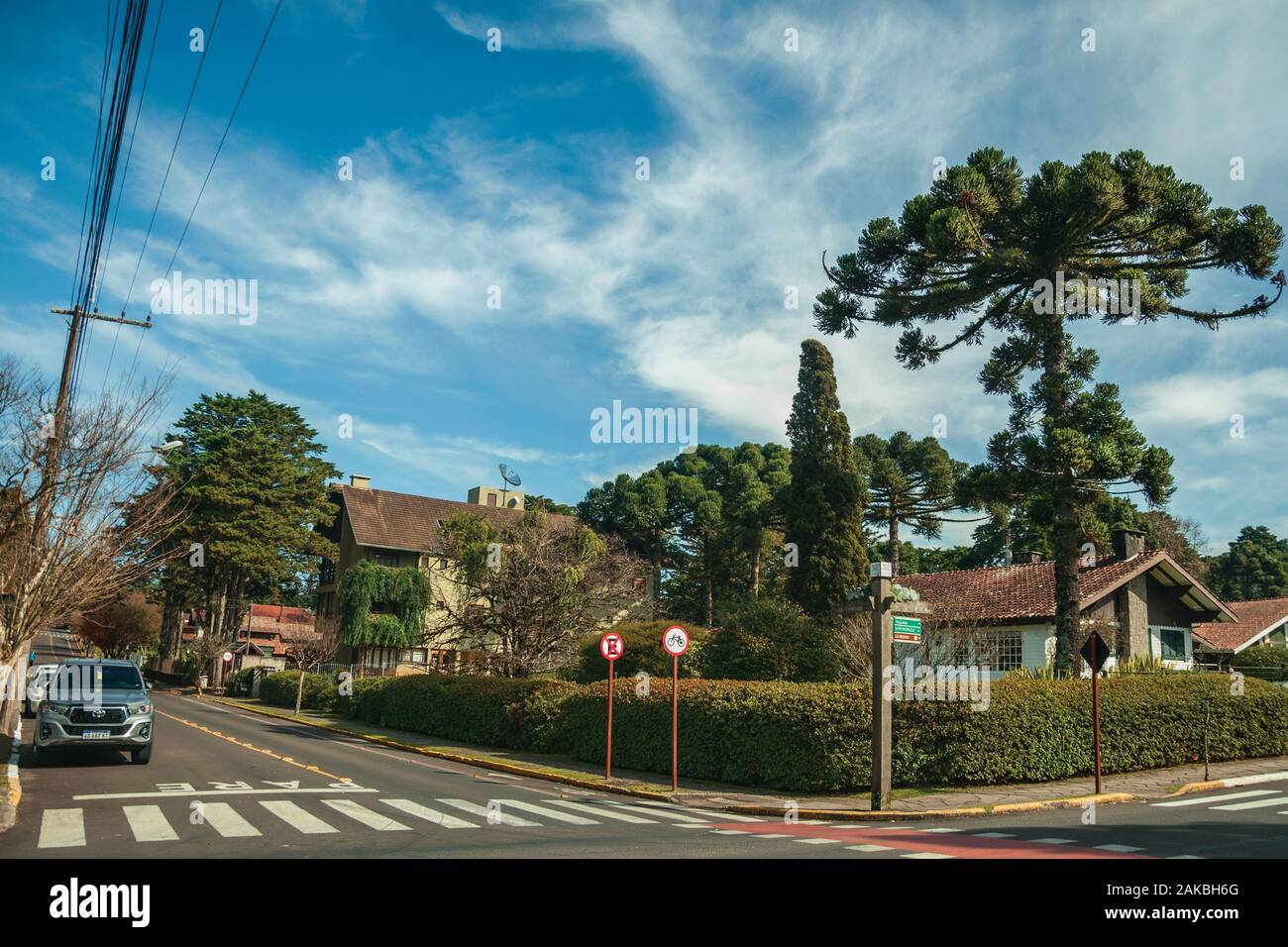 Begrünte Häuser und Bäume auf leere gepflasterte Strasse mit parkenden Autos an einem sonnigen Tag bei Gramado. Ein niedliches europäisch geprägten Stadt im südlichen Brasilien. Stockfoto