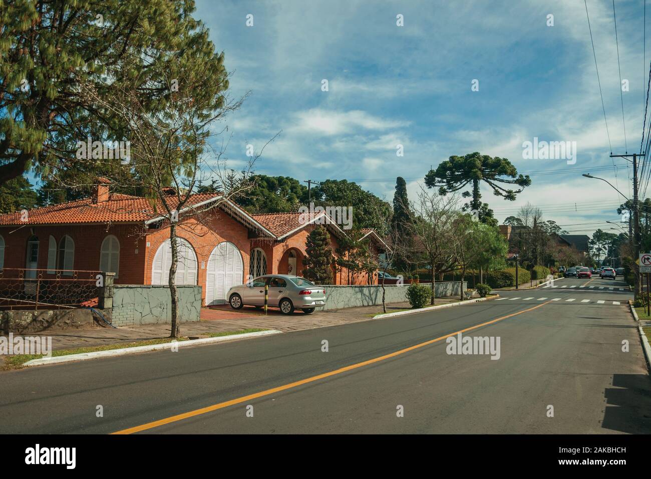 Begrünte Häuser und Bäume auf leere gepflasterte Strasse mit parkenden Autos an einem sonnigen Tag bei Gramado. Ein niedliches europäisch geprägten Stadt im südlichen Brasilien. Stockfoto