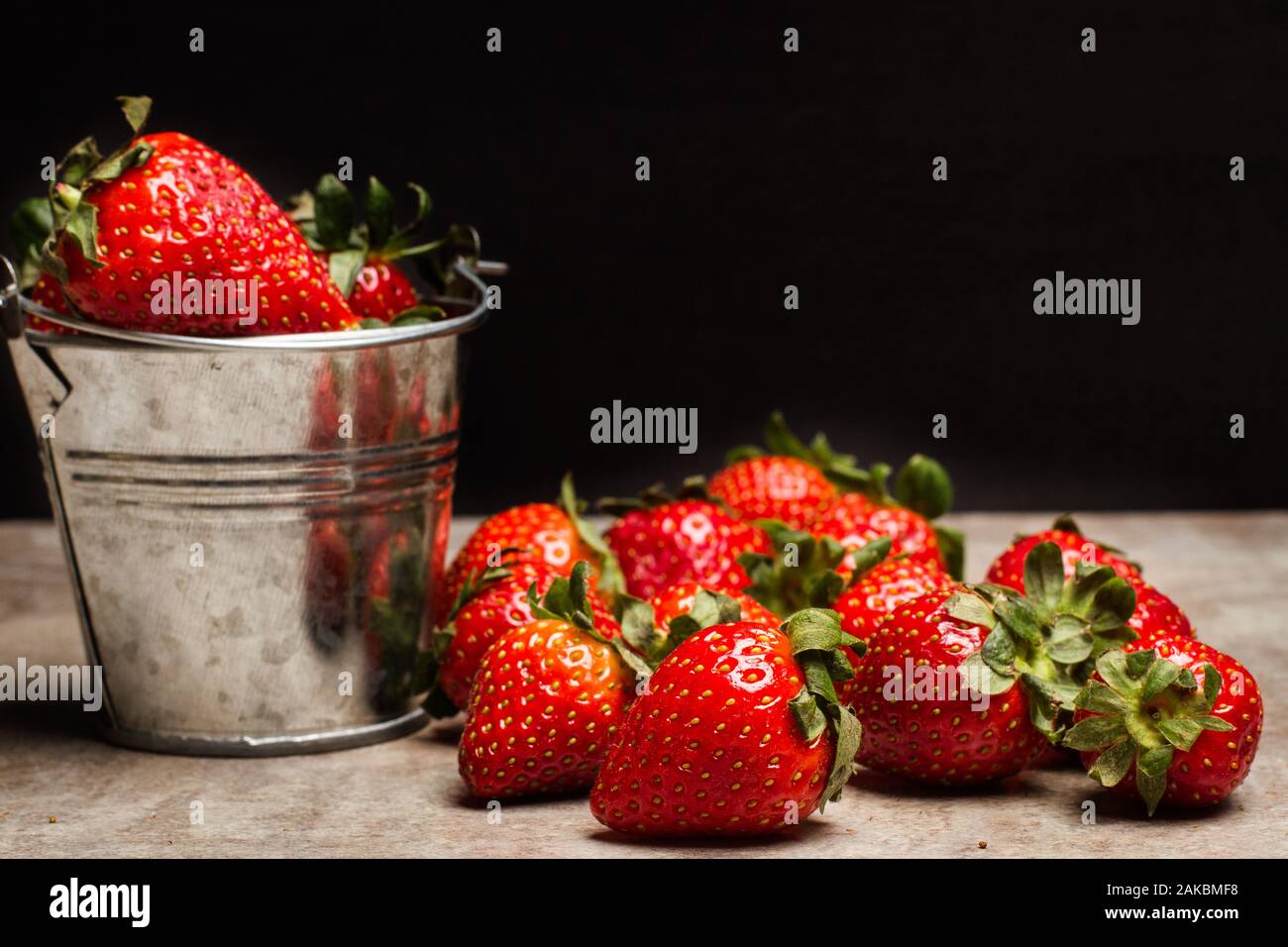 Lecker Erdbeeren in einem Eimer auf einem Marmortisch und auf einem dunklen Hintergrund Stockfoto
